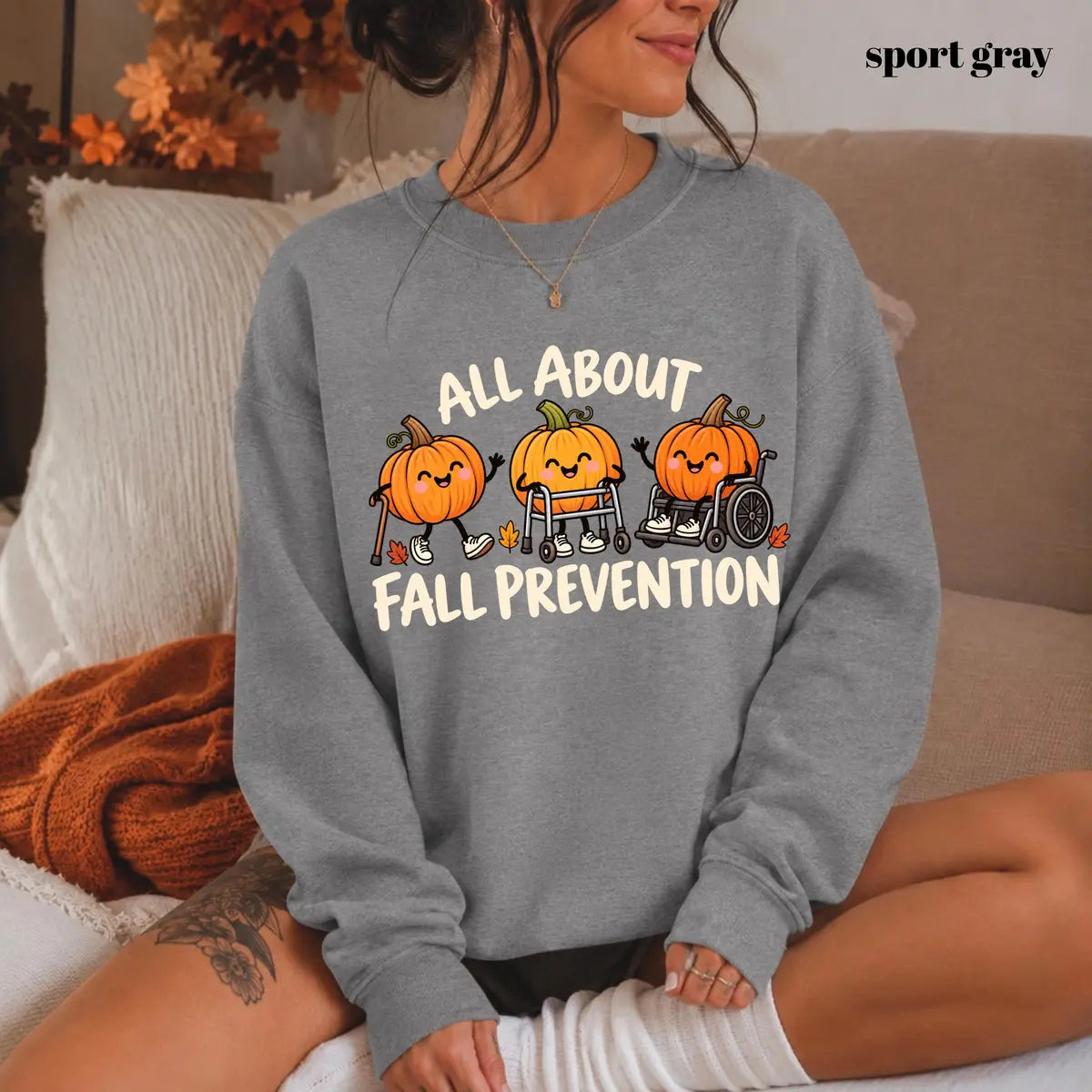 Sport Grey crewneck sweatshirt with printed pumpkins with a walker and wheelchair above the words all about fall prevention, worn by a model.