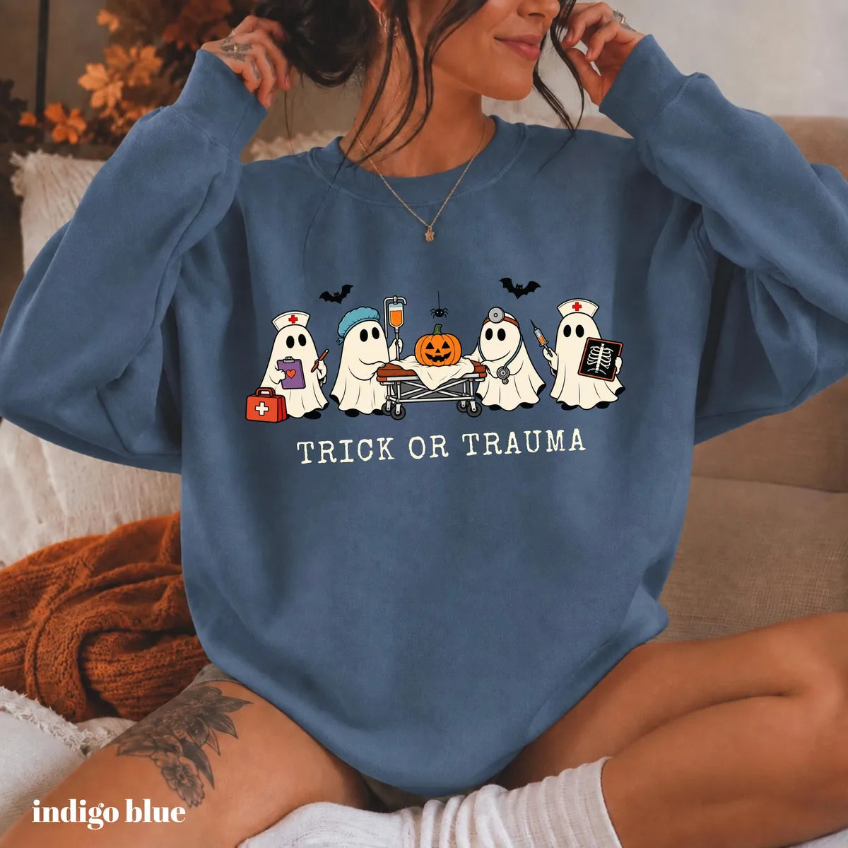 Indigo Blue crewneck sweatshirt with printed nurse ghosts with a pumpkin and the words trick or trauma, worn by a model.