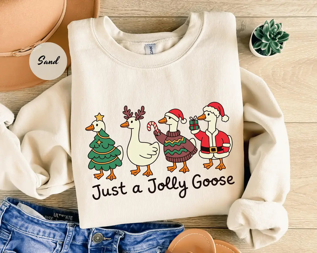 Sand crewneck sweatshirt with geese dressed as a Christmas tree, reindeer and Santa above the words just a jolly goose, flat lay view.