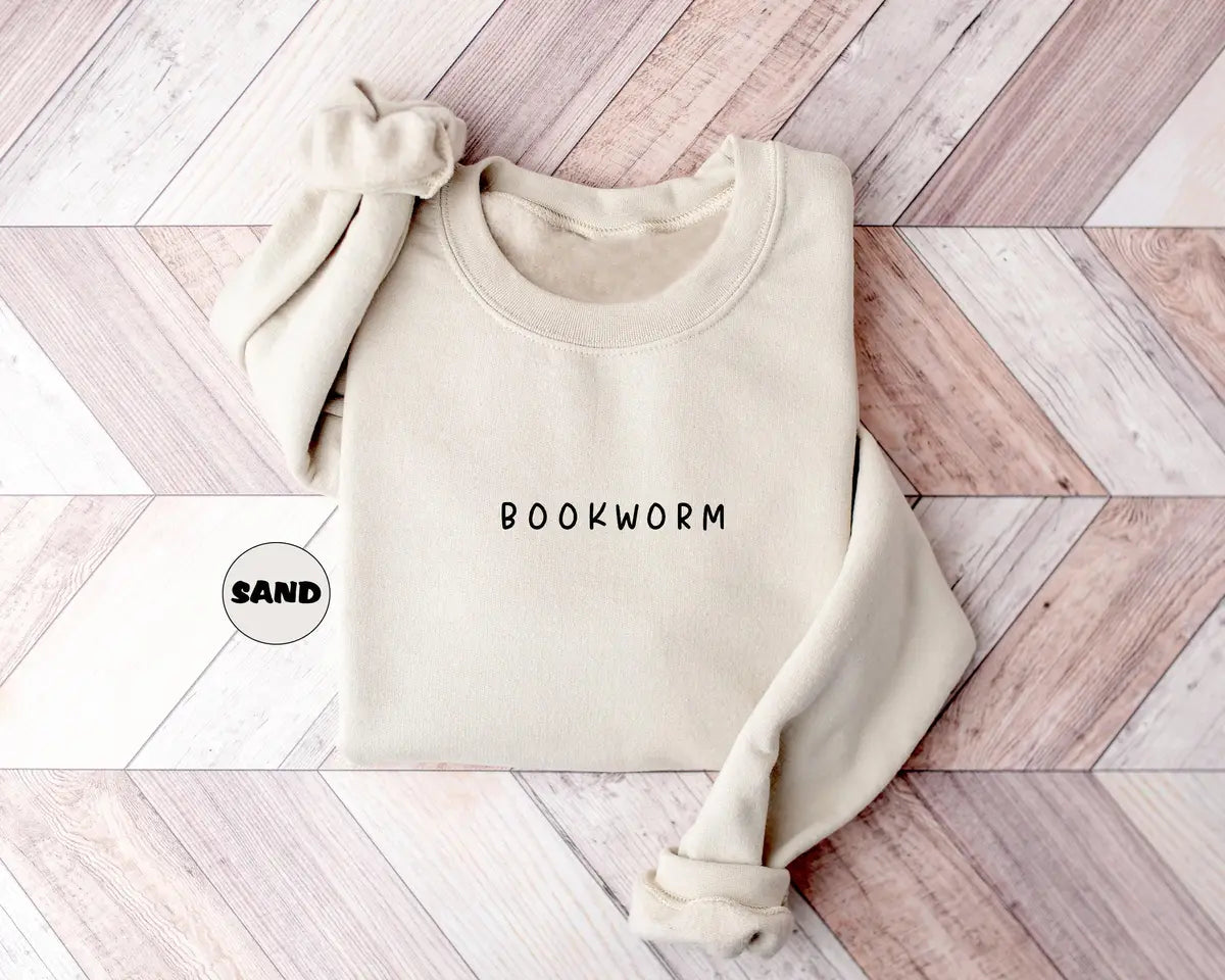Sand crewneck sweatshirt with small minimal lettering that reads bookworm on the chest, flat lay view.