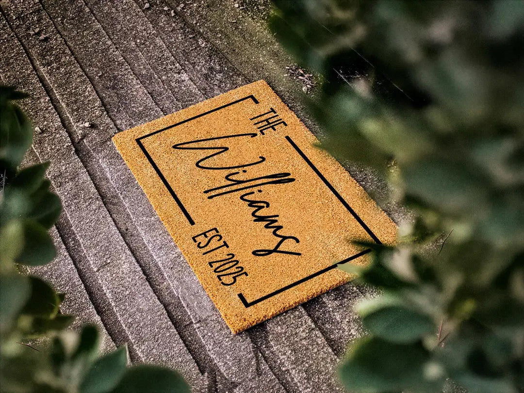Coir doormat with a framed family name and established year on weathered gray planks with leafy branches