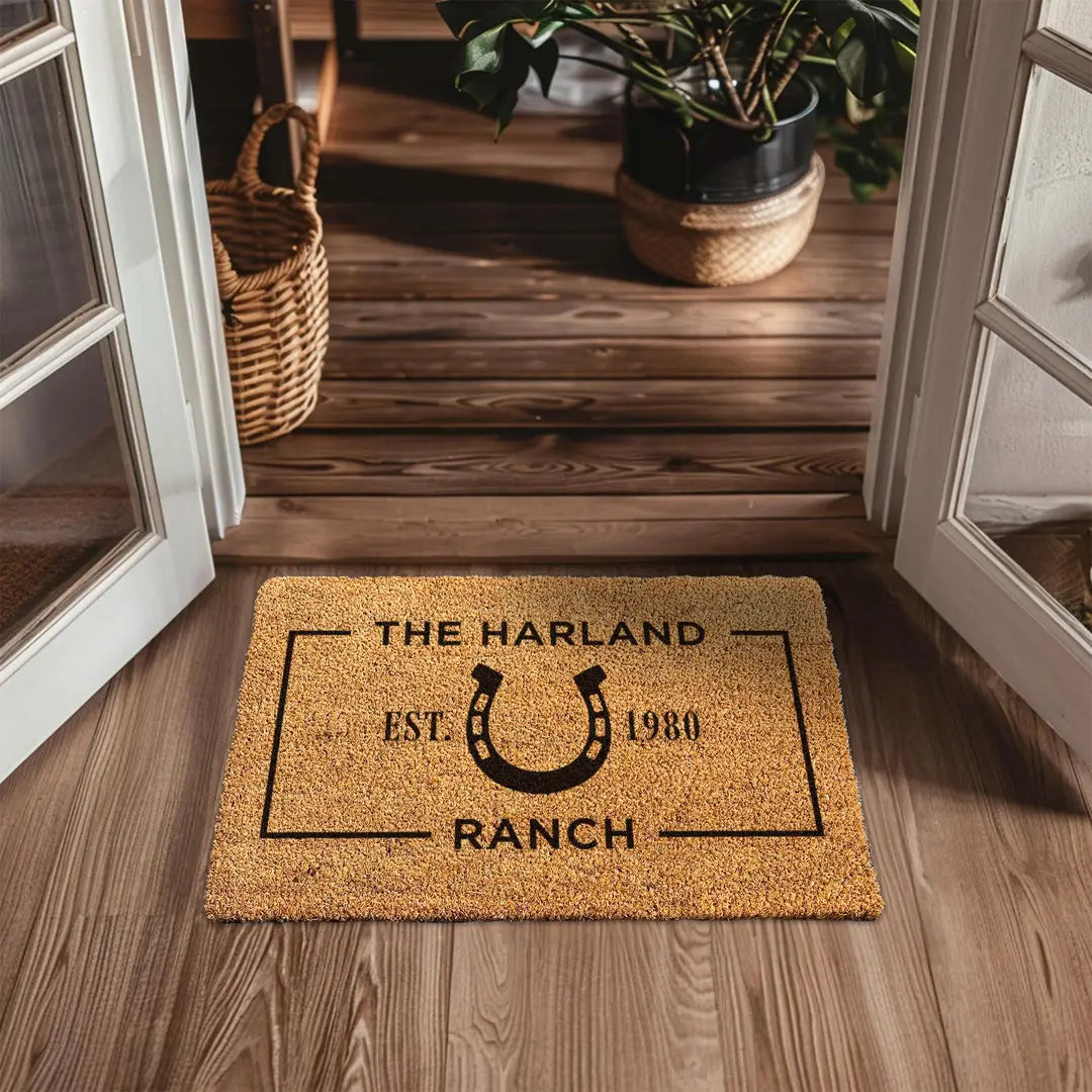Coir doormat with a horseshoe ranch design at a wooden entryway with white doors and a woven basket