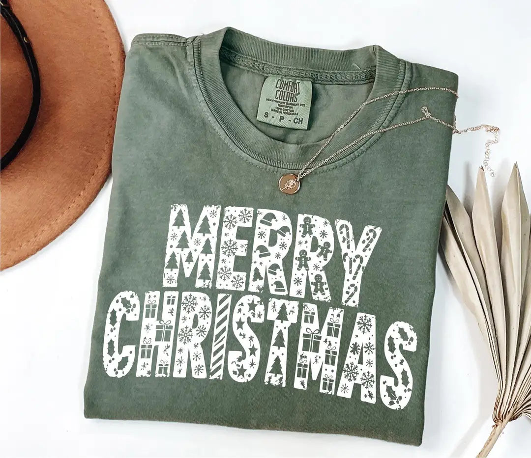 Folded moss-green Comfort Colors T-shirt with white patterned MERRY CHRISTMAS lettering.