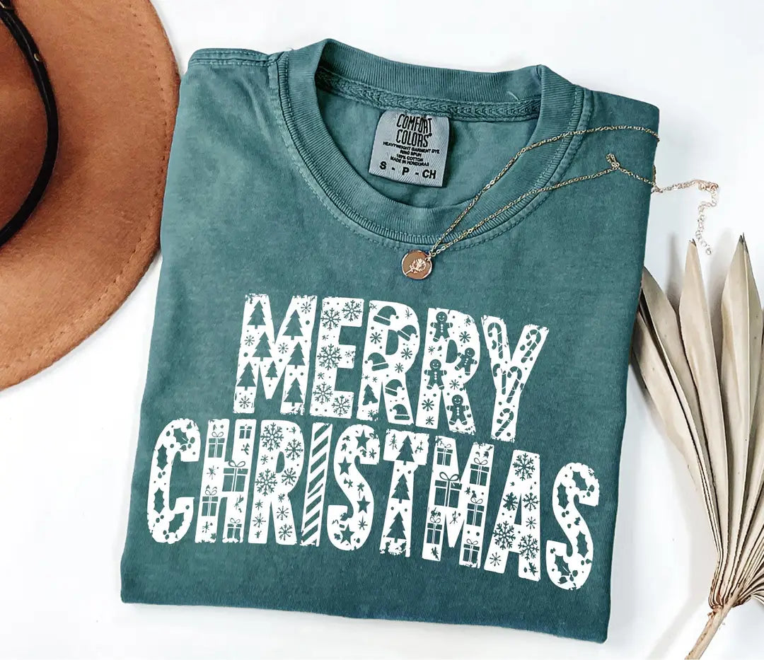 Blue Spruce Comfort Colors T-shirt with white patterned 'MERRY CHRISTMAS' holiday lettering.
