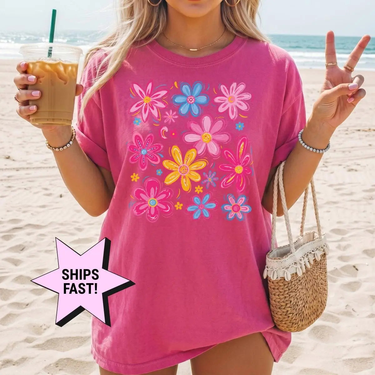 Woman in a Berry Comfort Colors tee on a beach with a straw bag and iced coffee, wildflower print on the chest