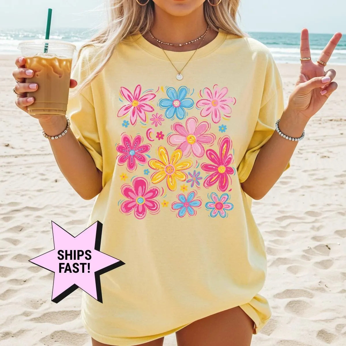 Woman in a Butter yellow Comfort Colors tee on a beach with an iced coffee, pink and blue wildflowers on the chest