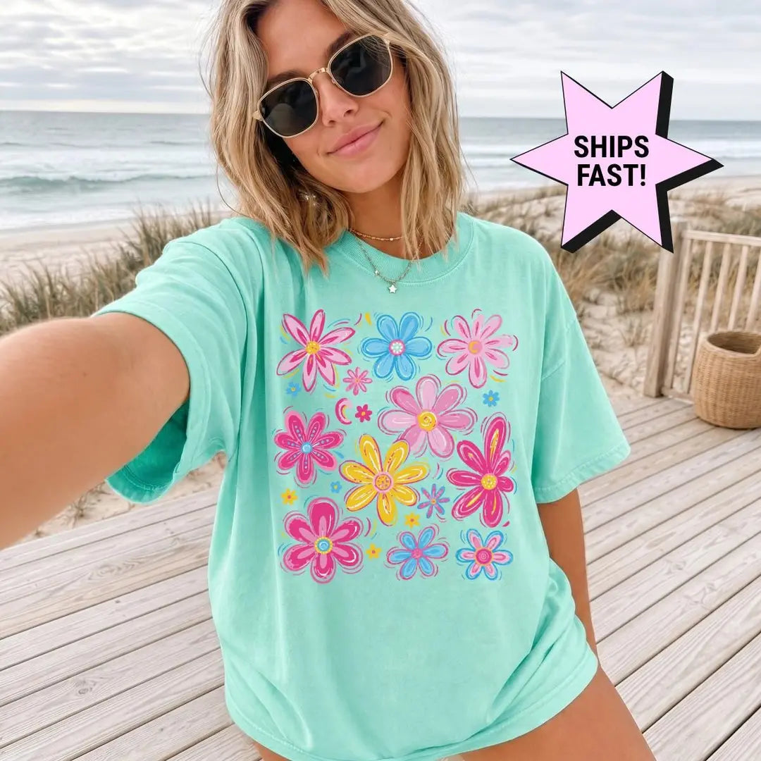 Woman in a Seafoam Comfort Colors tee taking a beach selfie in sunglasses, a cluster of bright wildflowers on the chest