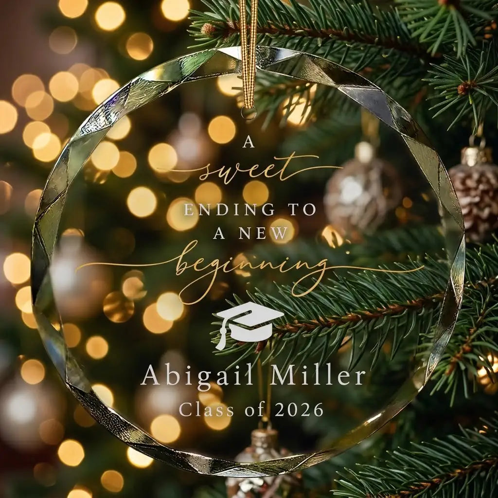 Personalized clear glass graduation ornament displayed hanging on Christmas tree branch with warm sparkling holiday lights background
