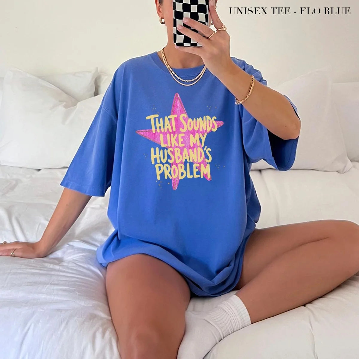 Woman in a Flo Blue Comfort Colors tee taking a mirror selfie on a bed, yellow husband's problem text on a pink star