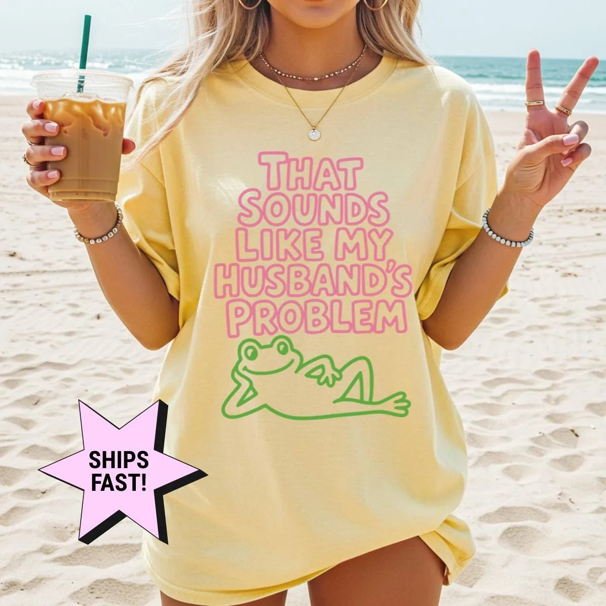 Woman in a Butter yellow Comfort Colors tee on a beach with an iced coffee, pink husband's problem text and a green frog