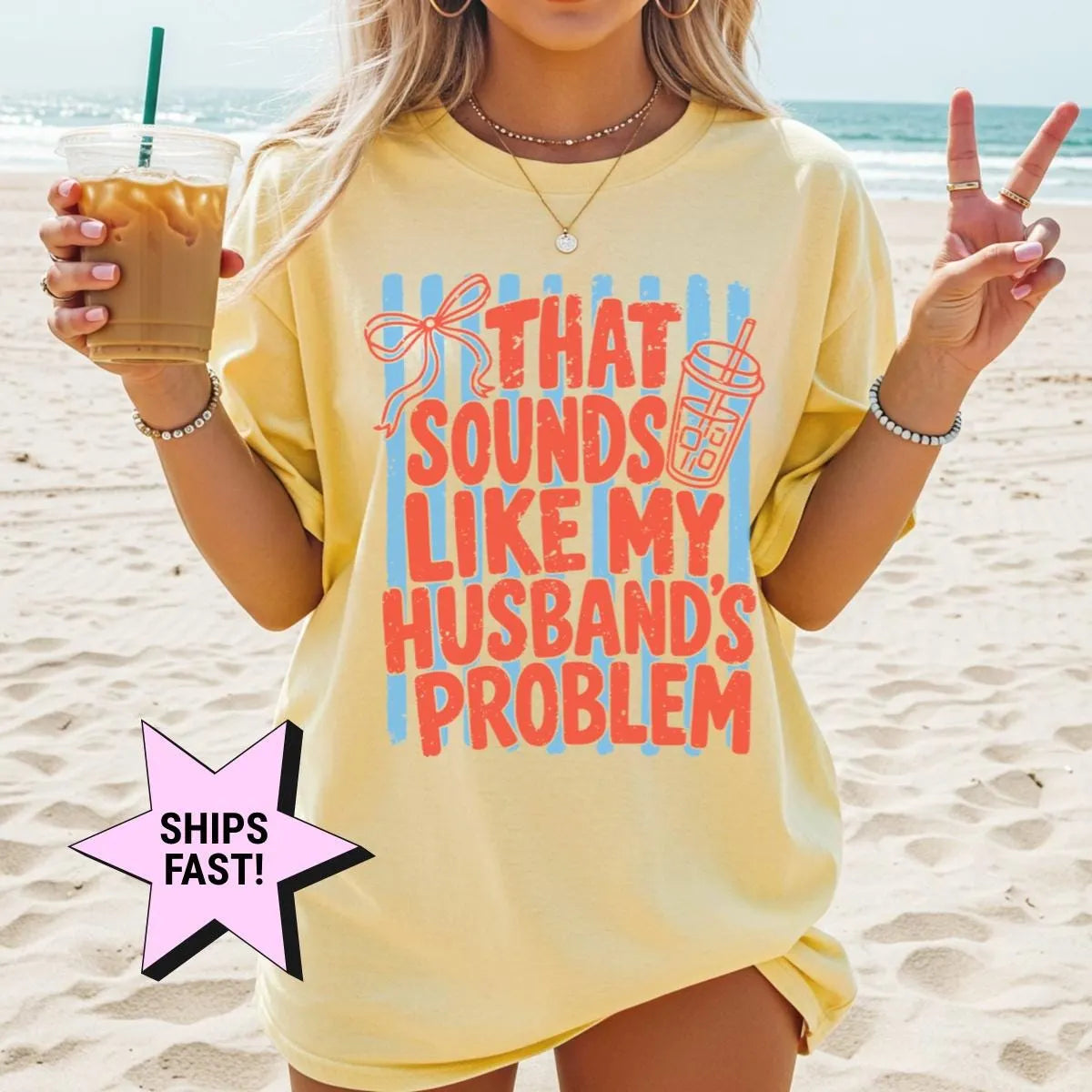 Woman in a Butter yellow Comfort Colors tee on a beach with an iced coffee, red husband's problem lettering on blue stripes