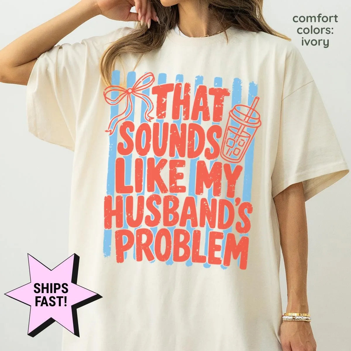 Woman in an Ivory Comfort Colors tee, hand at her hair, with red husband's problem block letters over light blue stripes
