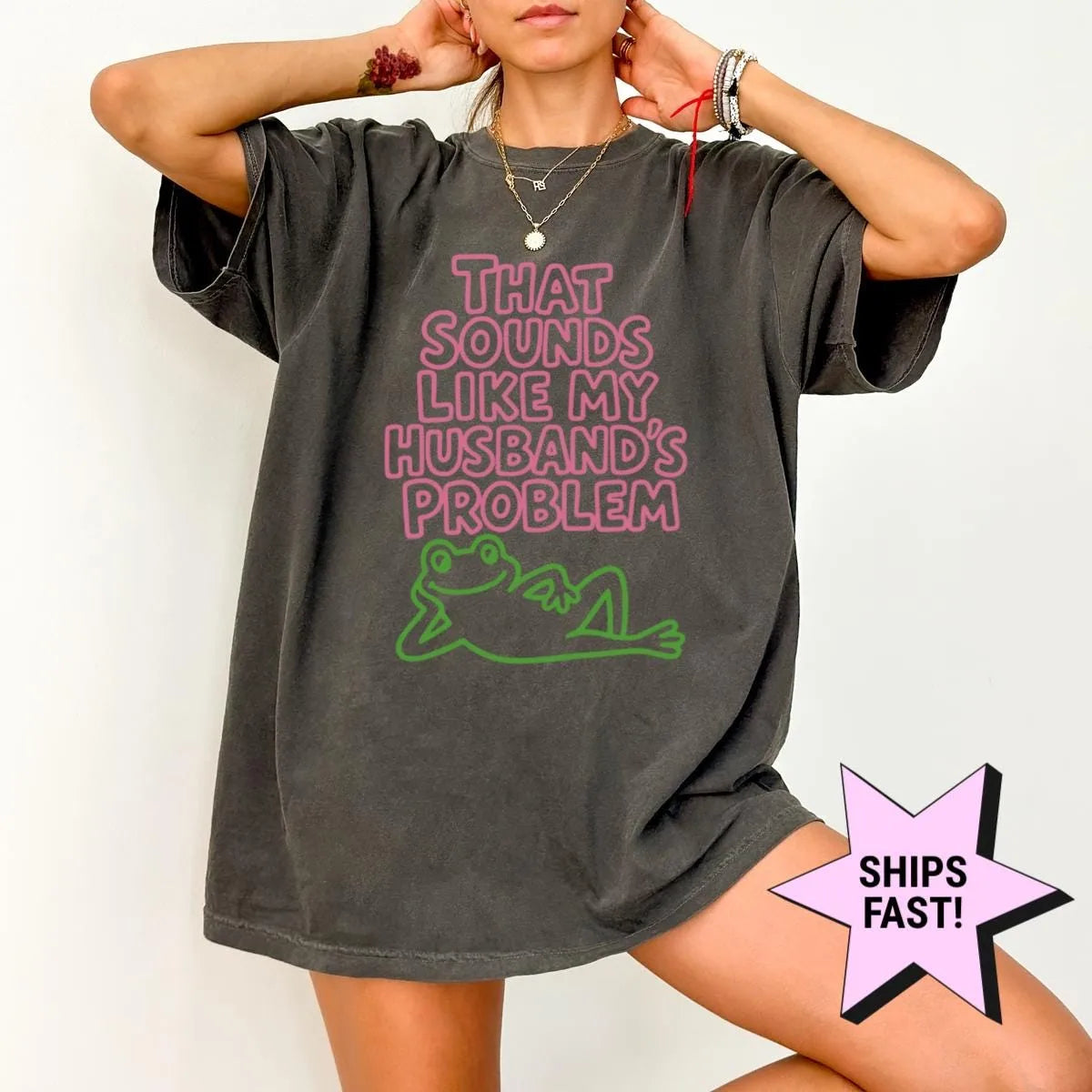 Woman in a Pepper Comfort Colors tee, hands behind her head, with pink outlined husband's problem text and a green frog