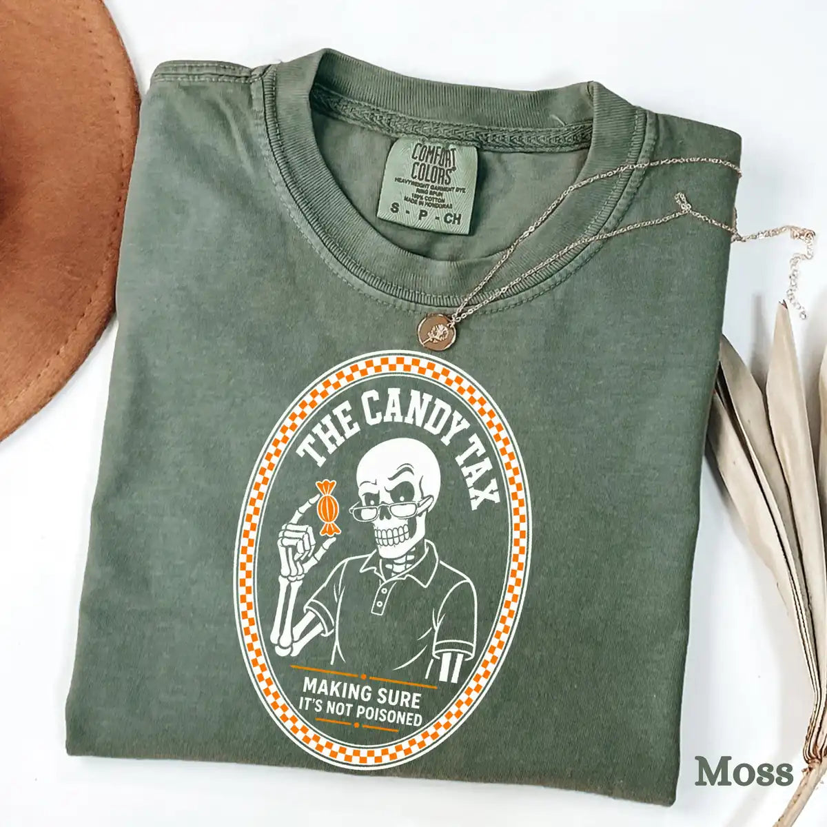 Comfort Colors T-shirt flatlay in Moss color featuring The Candy Tax skeleton dad holding candy graphic