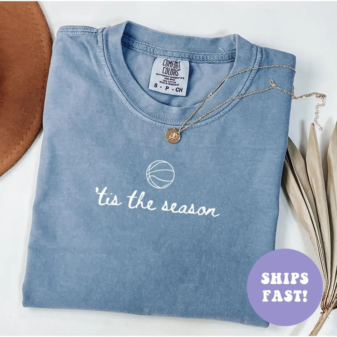 Folded Blue Jean Comfort Colors tee with a small white basketball above 'tis the season in cursive lettering