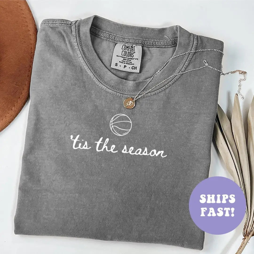Folded Pepper Comfort Colors tee with a basketball outline above 'tis the season in white cursive, necklace at the collar