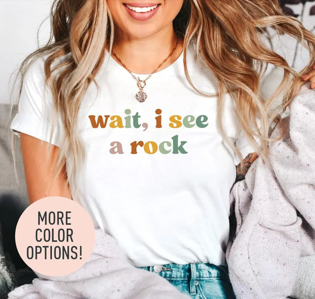 Woman in a white tee and a lilac cardigan, wait, i see a rock in two lines of mustard, sage and rose retro letters