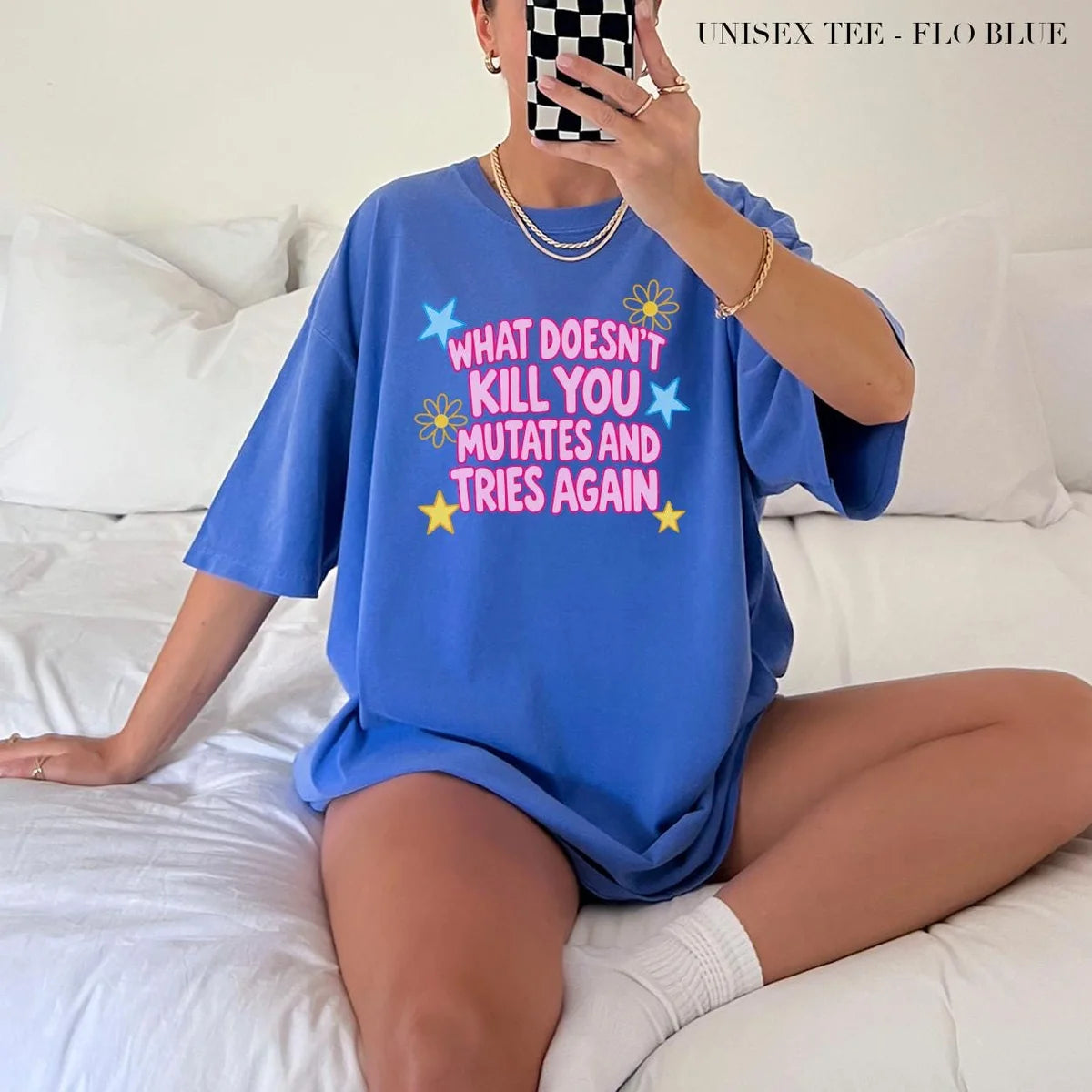 Woman in a Flo Blue Comfort Colors tee taking a mirror selfie on a bed, pink mutates and tries again lettering