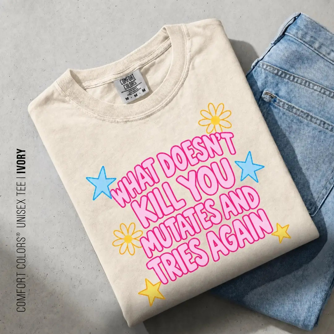 Folded Ivory Comfort Colors tee on blue jeans with pink what doesn't kill you mutates lettering and blue stars