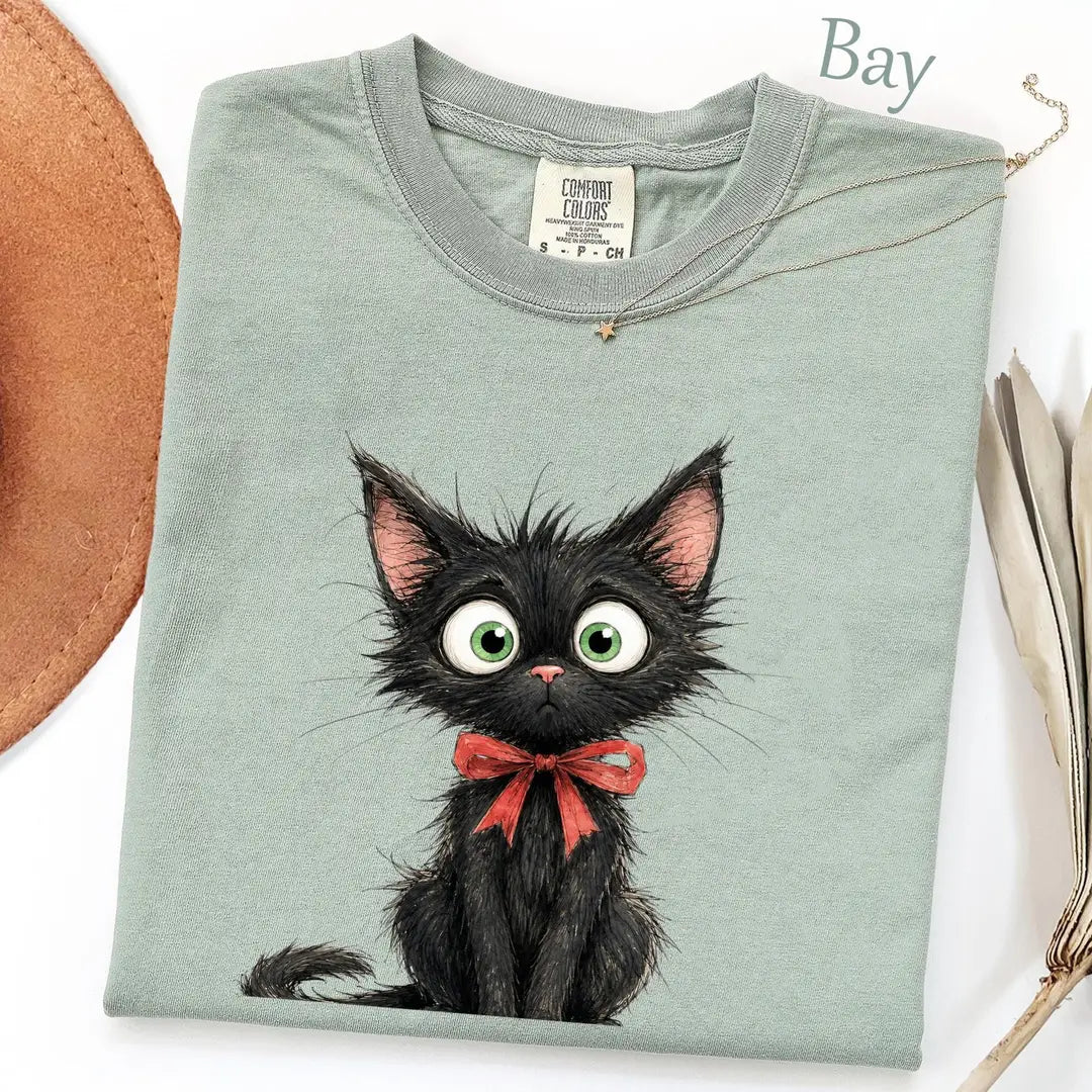 Folded Bay sage Comfort Colors tee with a large scruffy black kitten, big green eyes and a red bow, necklace on collar