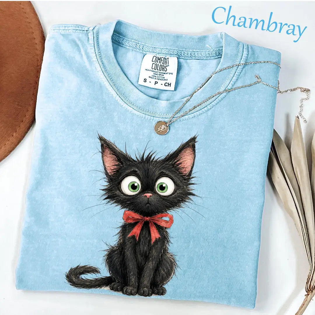 Folded Chambray blue Comfort Colors tee with a scruffy black kitten, round green eyes and a red bow under the neck