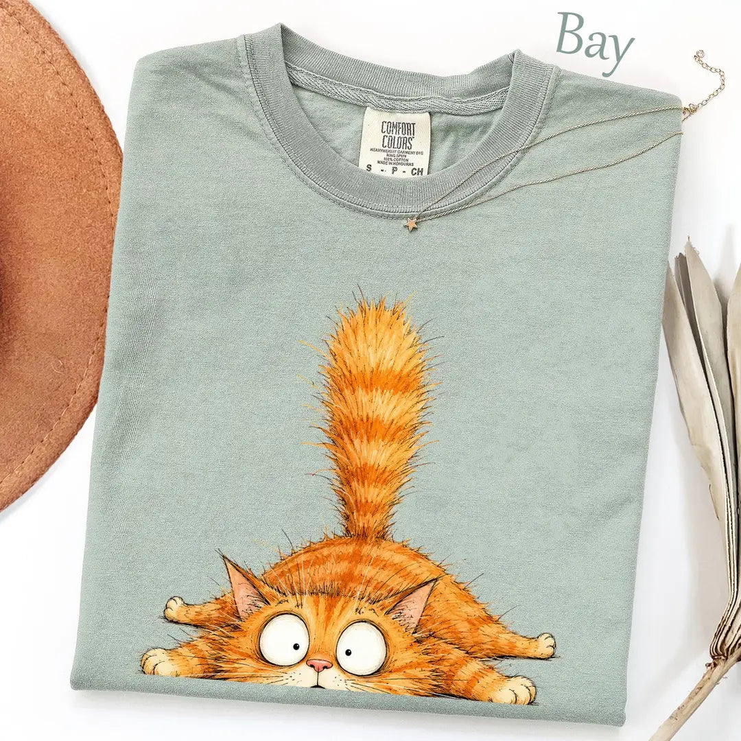 Folded Bay sage Comfort Colors tee with a sprawled orange tabby, wide googly eyes and a tall striped tail