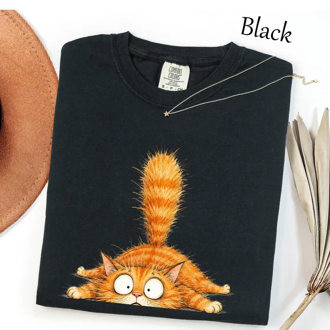 Folded Black Comfort Colors tee with an orange tabby sprawled flat, bulging eyes and a fluffy upright tail, necklace above