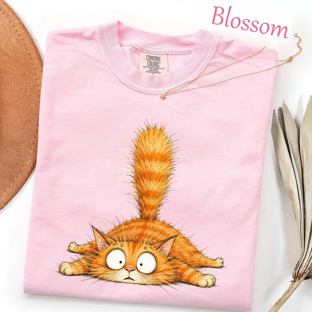 Folded Blossom pink Comfort Colors tee with a fluffy orange tabby lying flat, googly eyes and its tail straight up
