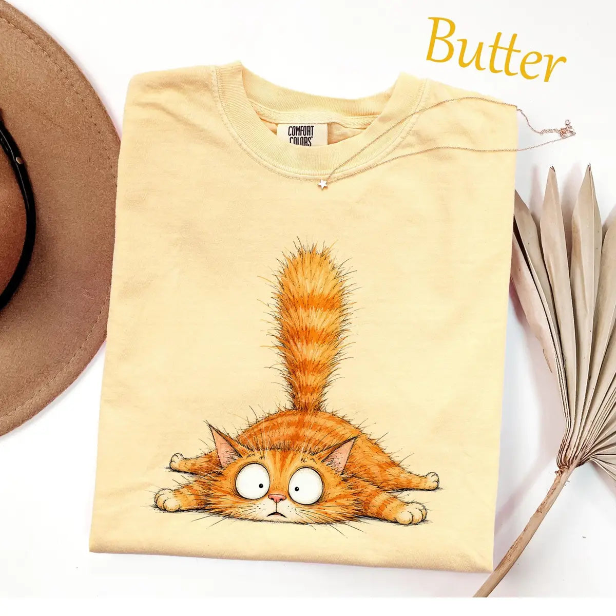 Folded Butter yellow Comfort Colors tee with a sprawled orange tabby with wide round eyes and its tail straight up