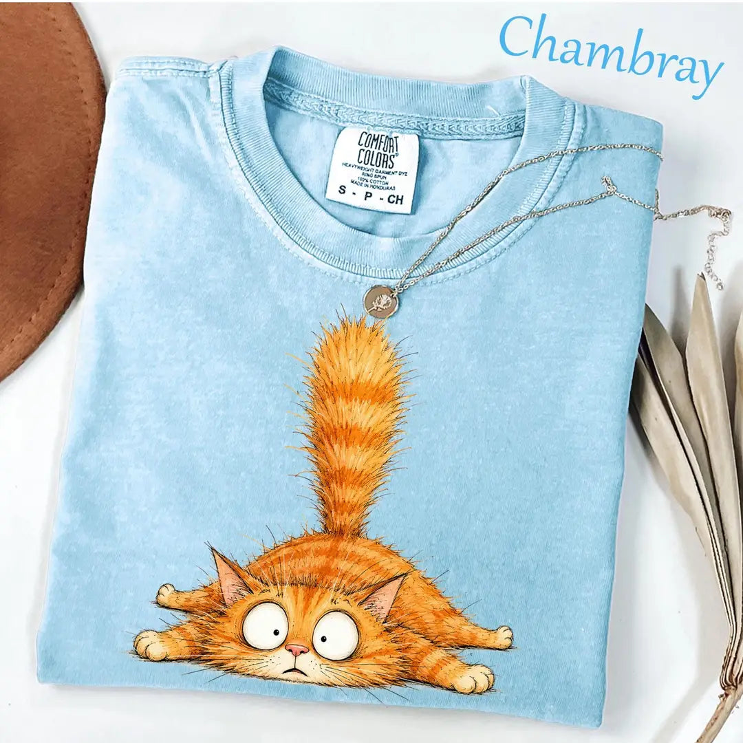 Folded Chambray blue Comfort Colors tee with a sprawled orange tabby cat, wide googly eyes and its tail in the air