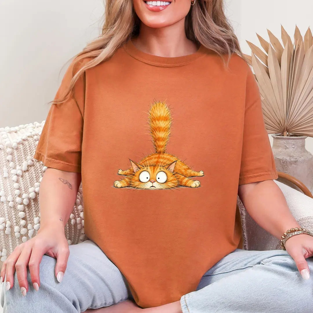 Woman in a Yam orange Comfort Colors tee sitting on a couch, a small orange tabby with googly eyes on the chest