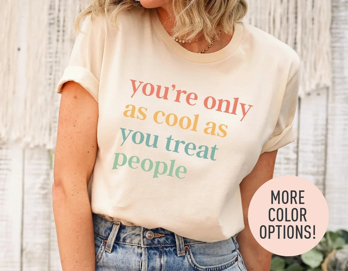 Woman in a natural cream tee with rolled sleeves and jeans, you're only as cool as you treat people in coral and sage