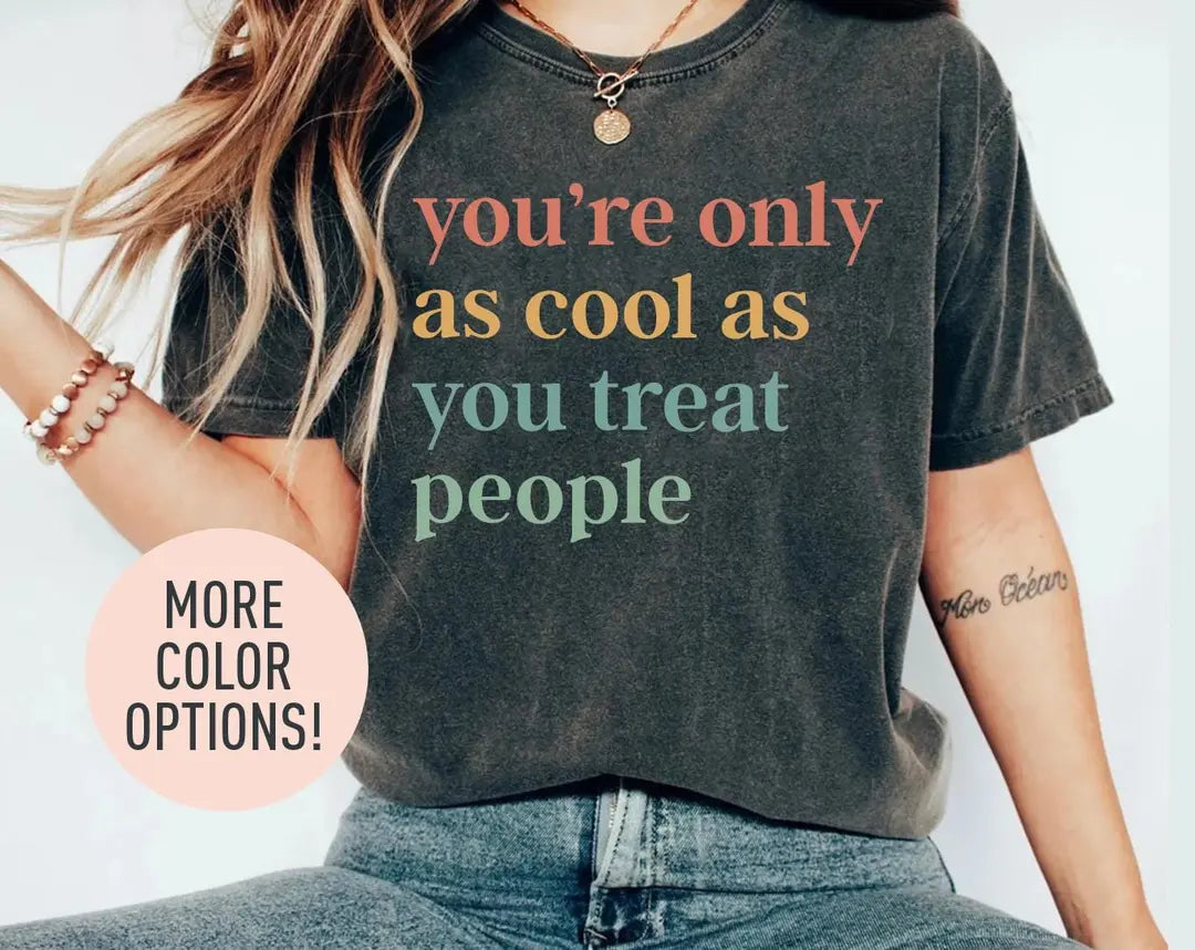 Woman in a dark gray Comfort Colors tee and jeans, bracelets, with a four-line you're only as cool as you treat people quote